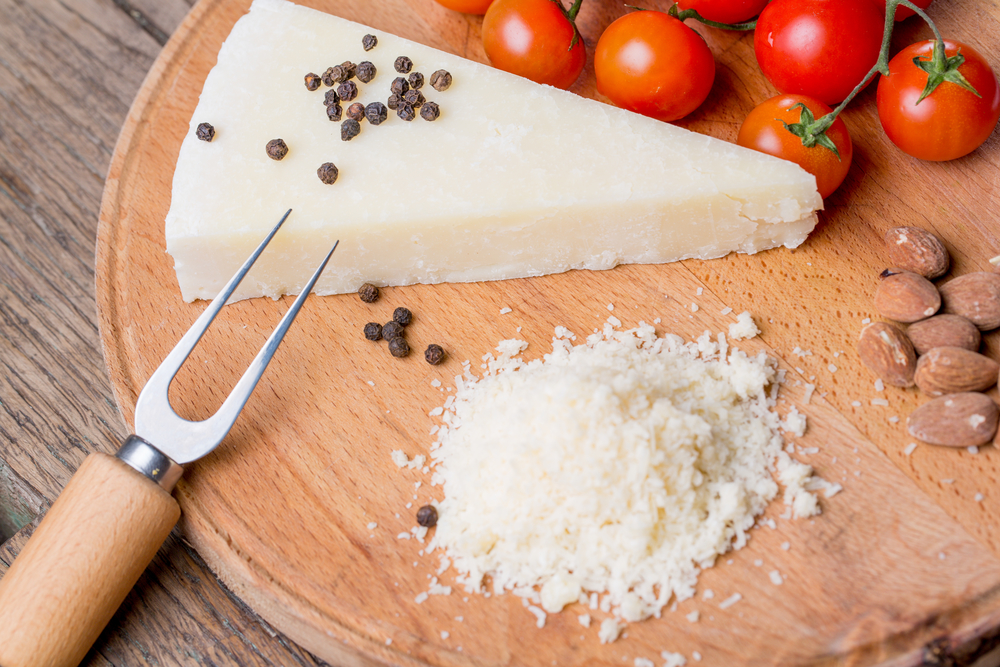 Grated pecorino cheese on wooden cutting board with tomatoes, selective focus.