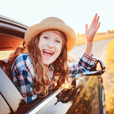 happy child girl looking out the car window during road trip on summer vacations. Summertime, exploring new places concept