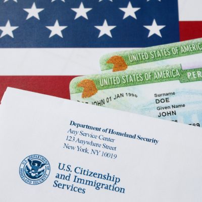 United States Permanent resident green cards from dv-lottery lies on United States flag with envelope from Department of Homeland Security close up