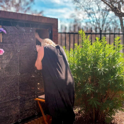 Daughter grieving at father’s resting place outdoors.