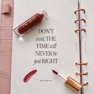 Prakti Beauty lip oil styled on a blush pink planner with an inspirational quote.